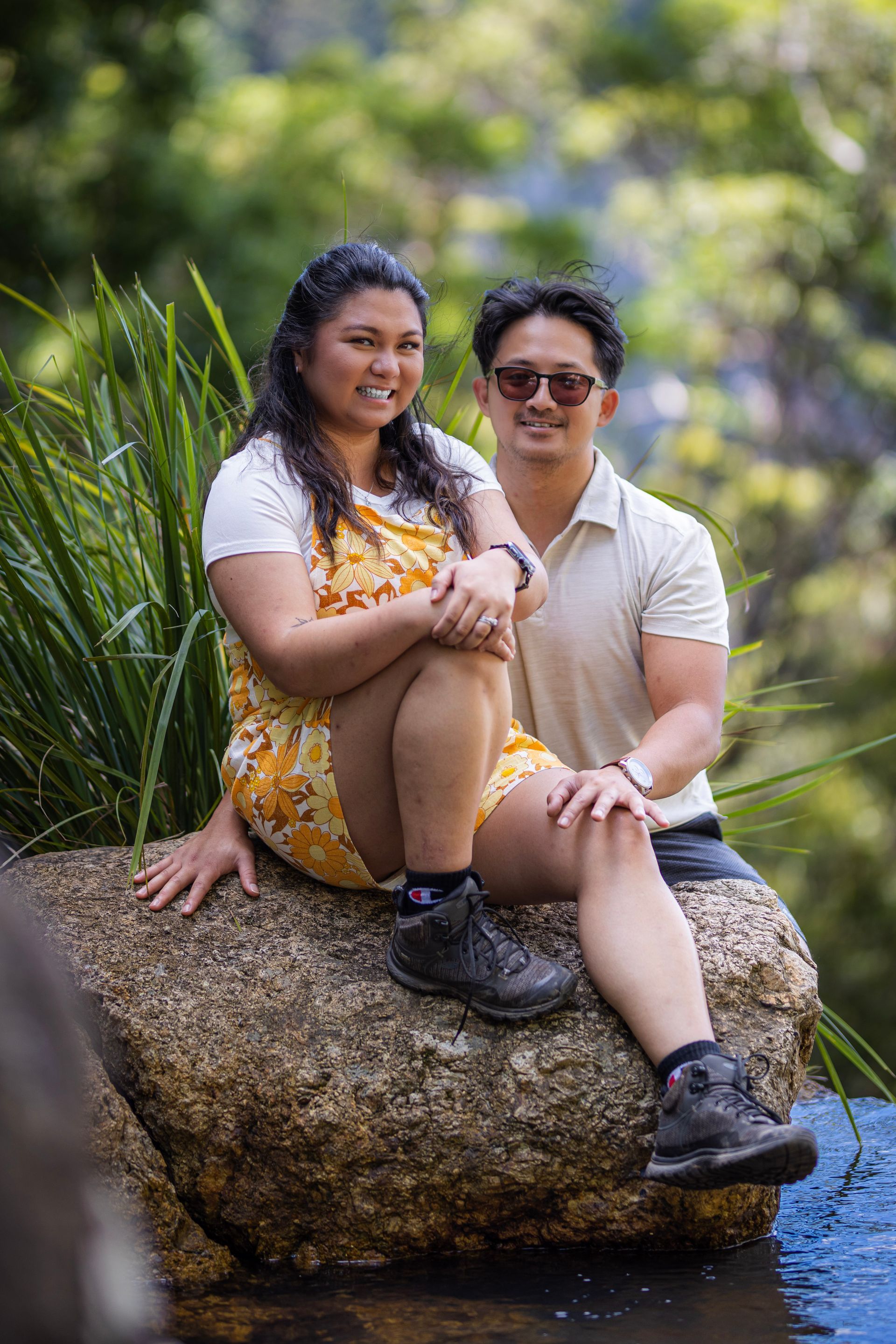 a man and a woman are sitting on a rock next to a pond .