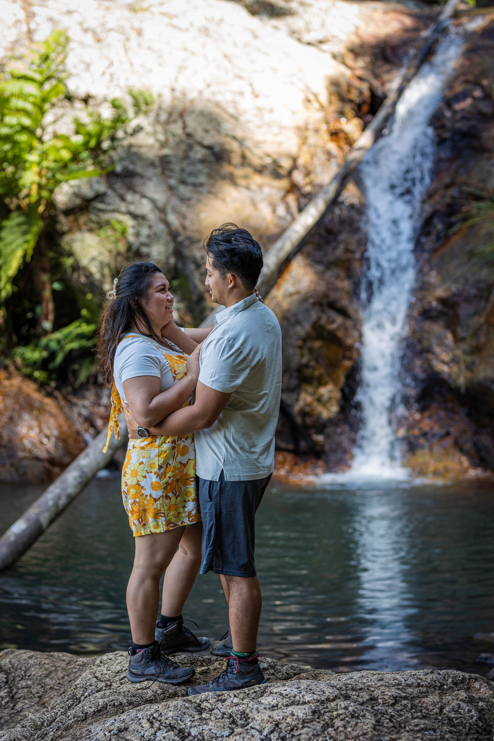 a man and a woman are standing in front of a waterfall .