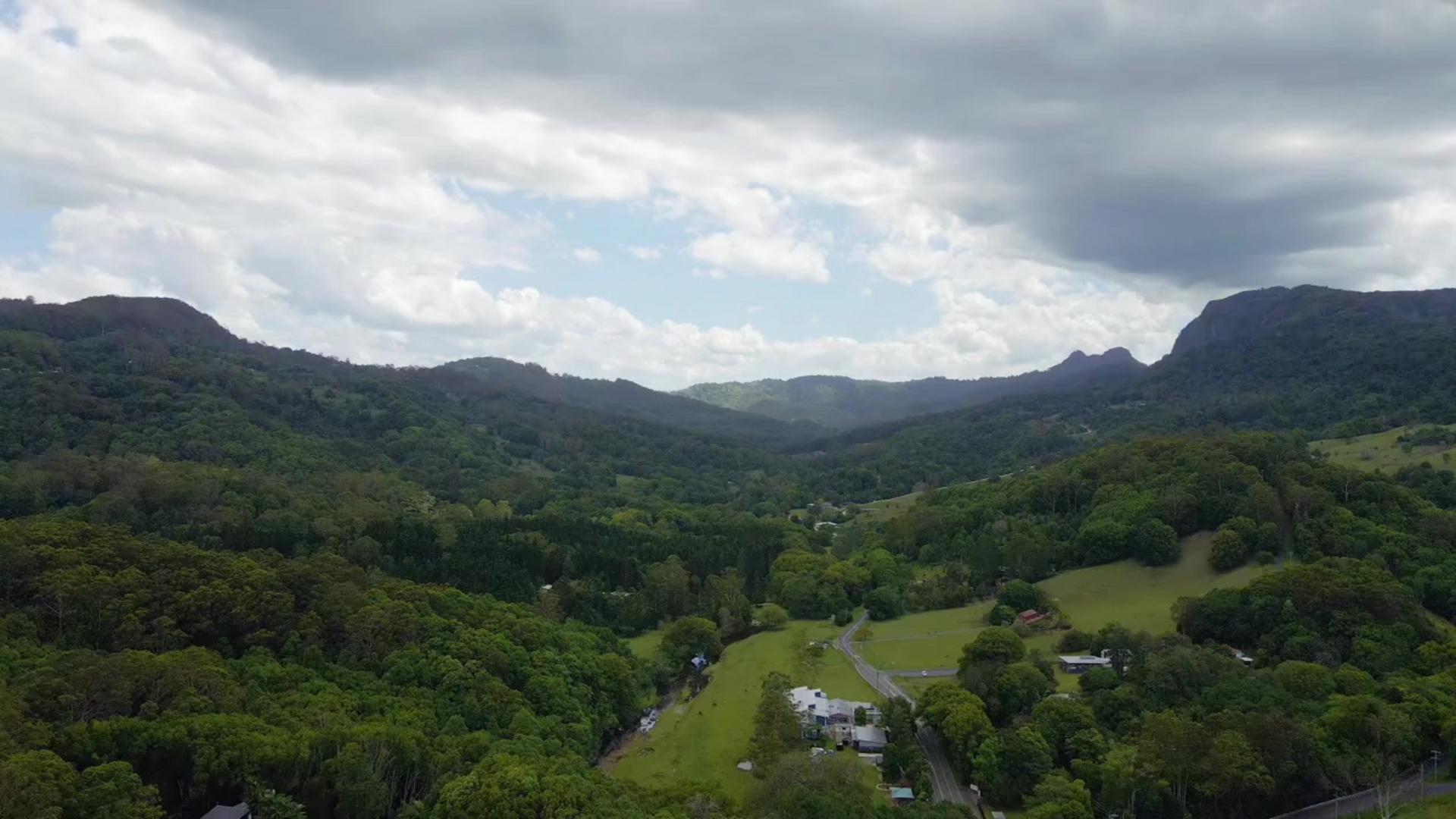 An aerial view of a south east queensland valley filled with trees and mountains on a cloudy day.