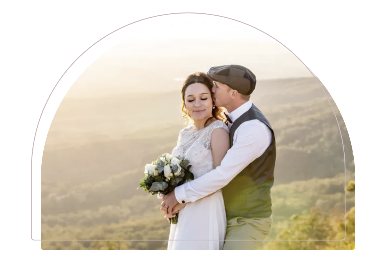 Couple embracing in wedding attire outdoors at sunset, with a soft golden landscape background
