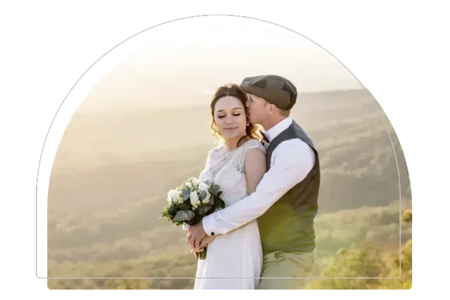 Couple embracing in wedding attire outdoors at sunset, with a soft golden landscape background