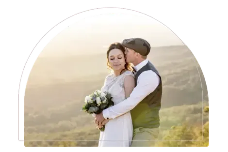 Couple embracing in wedding attire outdoors at sunset, with a soft golden landscape background