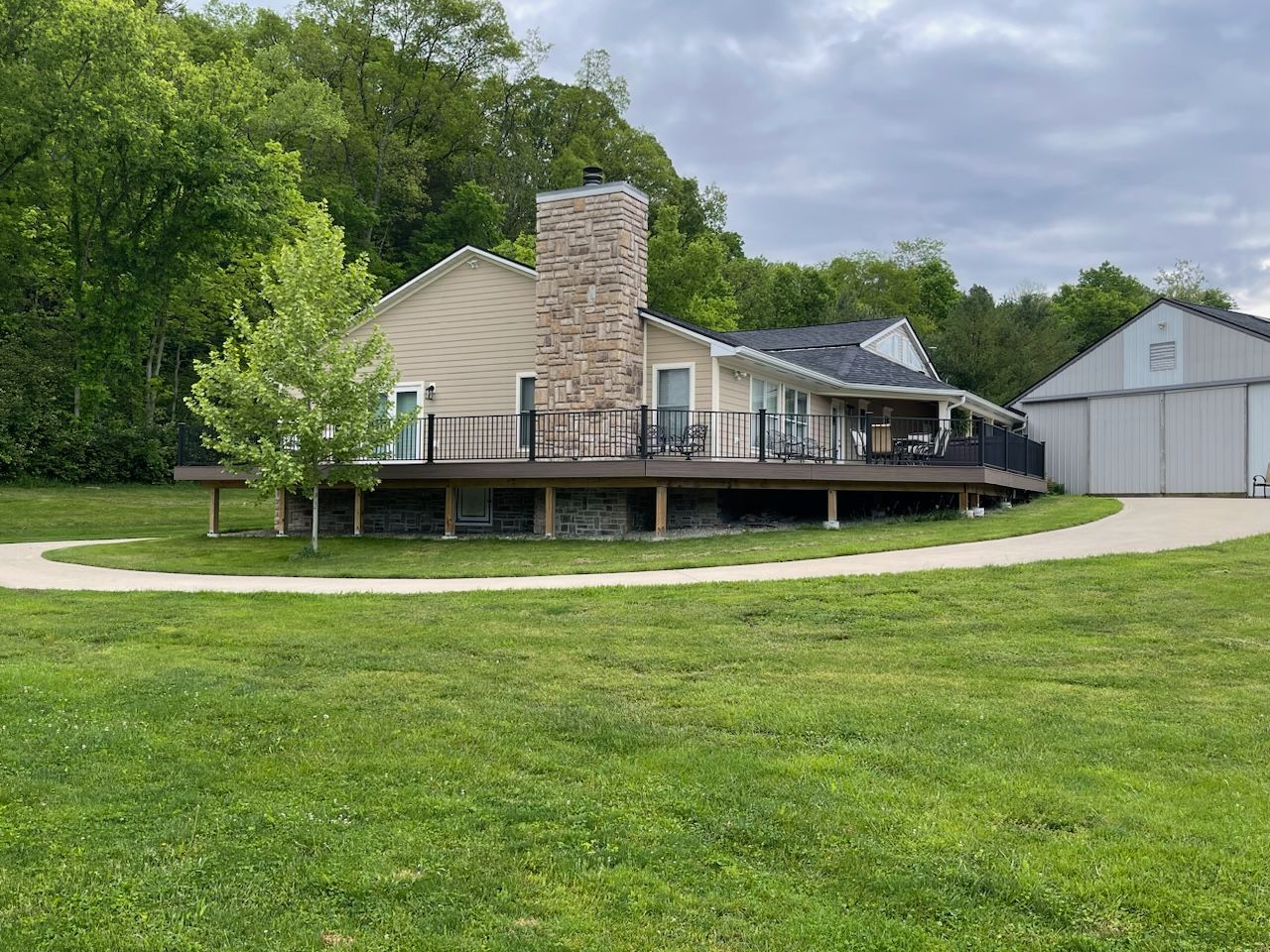 A house with a large deck and a garage is sitting on top of a lush green field.