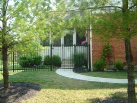 A brick house with a wrought iron fence and trees in front of it.