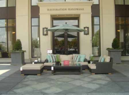 A patio with furniture and an umbrella in front of a building that says restoration hardware
