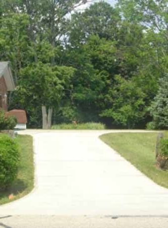 A concrete driveway leading to a house surrounded by trees.