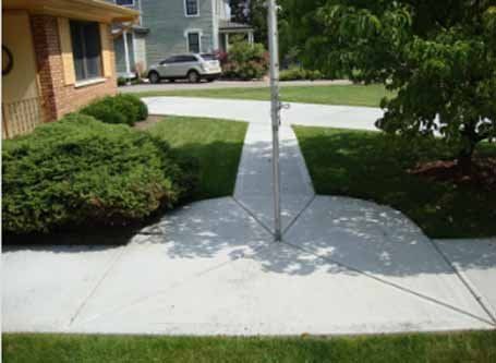 A concrete walkway leading to a house with a flag pole in the middle.