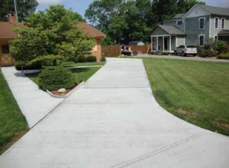 A concrete driveway leading to a house with a lush green lawn.