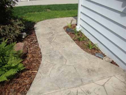 A concrete walkway leading to a house with a white house in the background.