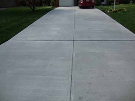 A red car is parked on the side of a concrete driveway.