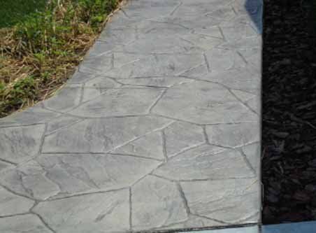 A concrete walkway with a stone pattern and a grassy area in the background.
