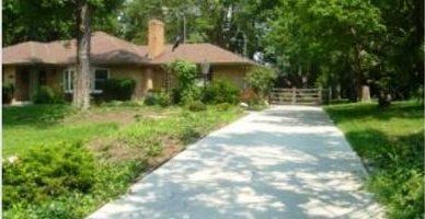 A concrete driveway leading to a house surrounded by trees.