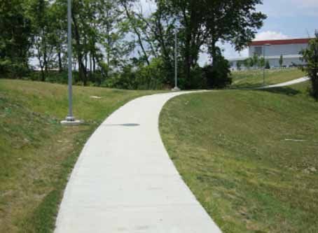 A concrete walkway going through a grassy field.