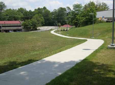 A concrete walkway going through a grassy field.