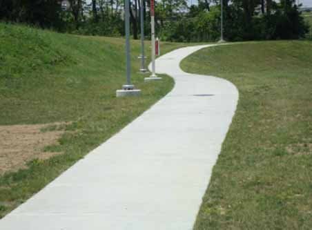 A concrete walkway going through a grassy field.