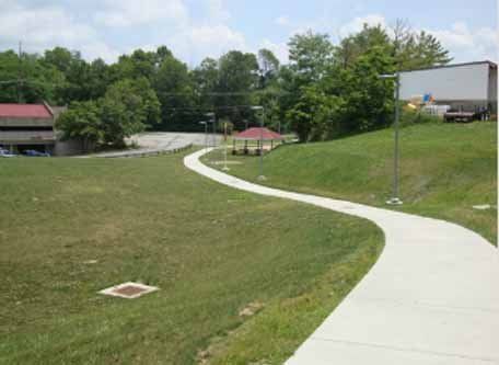 A concrete walkway going through a grassy field.