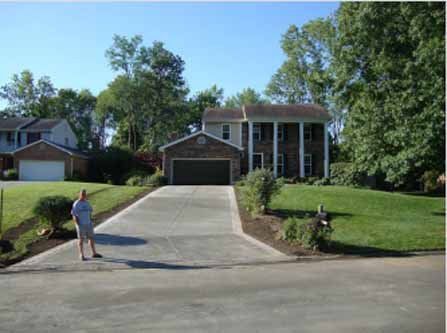 A man is standing in the driveway of a house.