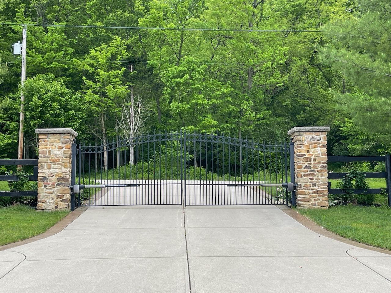 A concrete driveway with a wrought iron gate and a stone pillar.