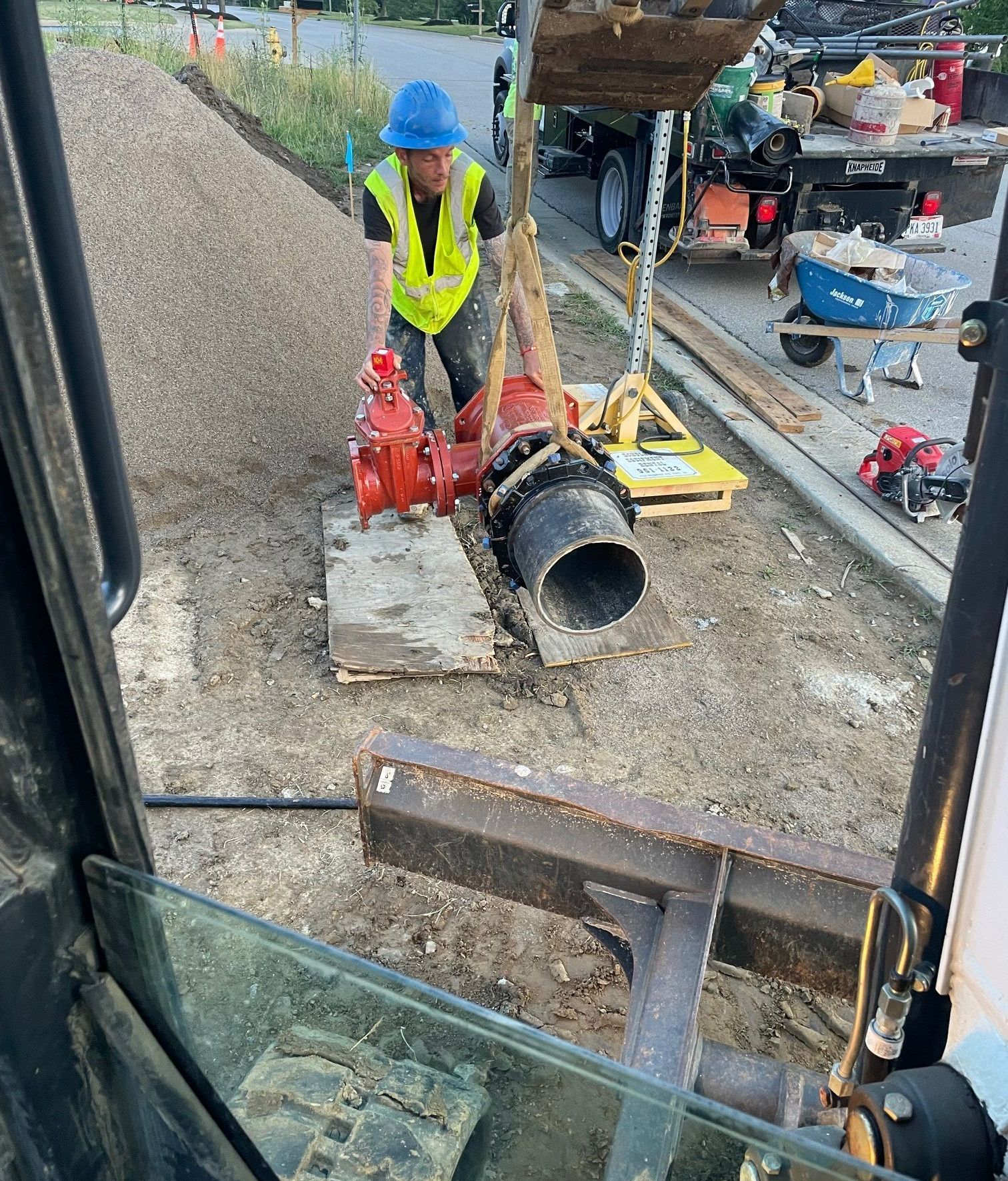 A man in a yellow vest and blue hat is working on a pipe.