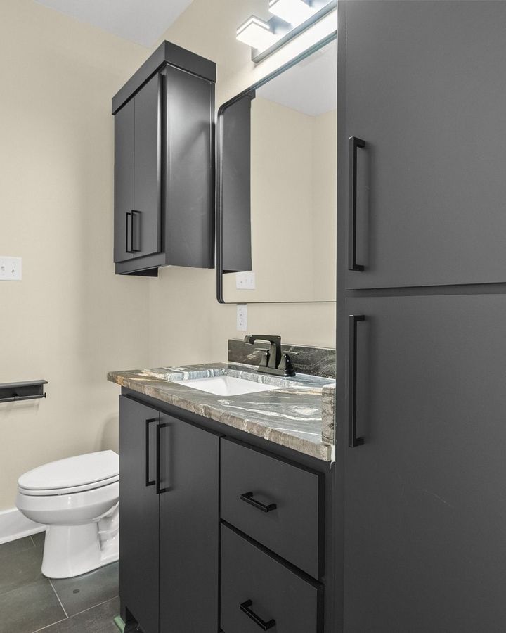 Modern bathroom vanity with dark cabinets, granite countertop, mirror, and toilet on the left.