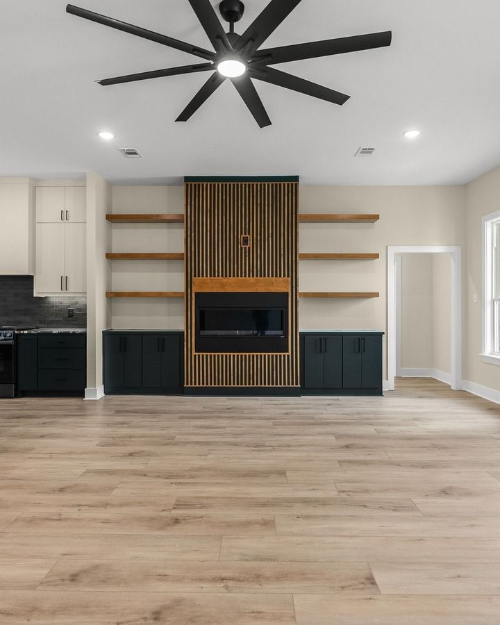 Modern living room with wood floors, built-in shelving, black ceiling fan, and central fireplace wall panel.