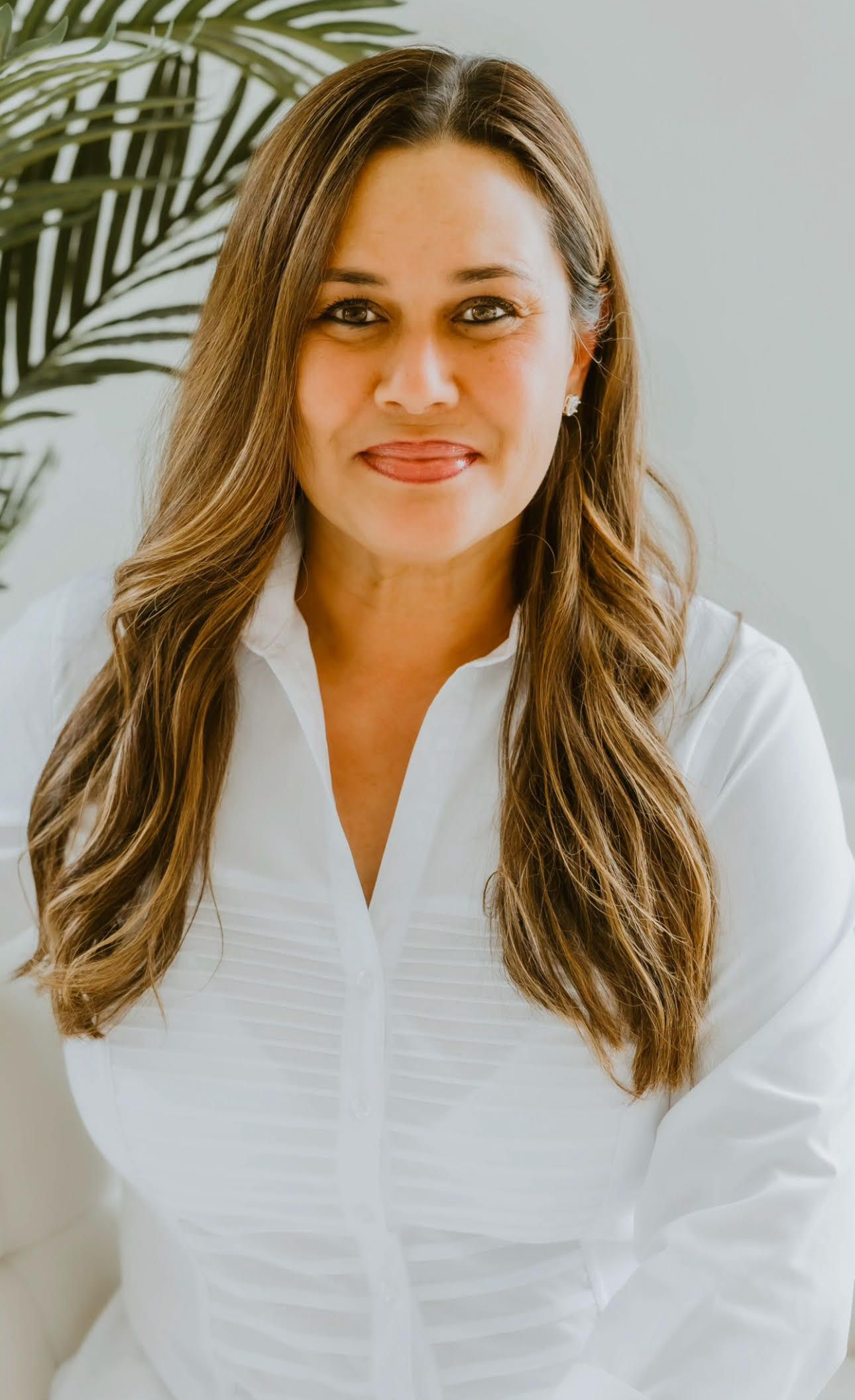 Woman in a white blouse smiling in a bright indoor setting.