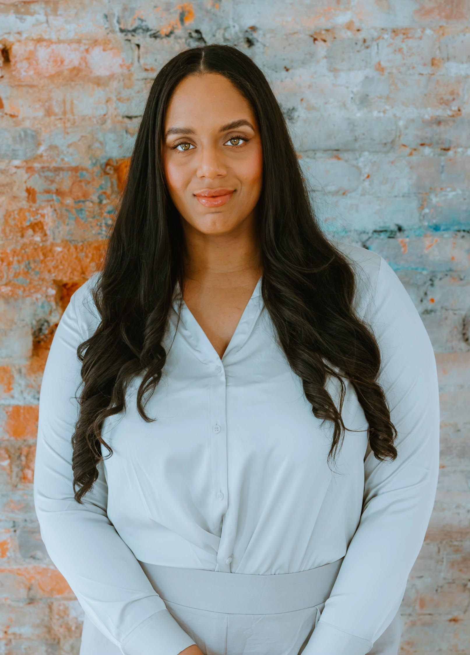 A woman with long hair is standing in front of a brick wall.