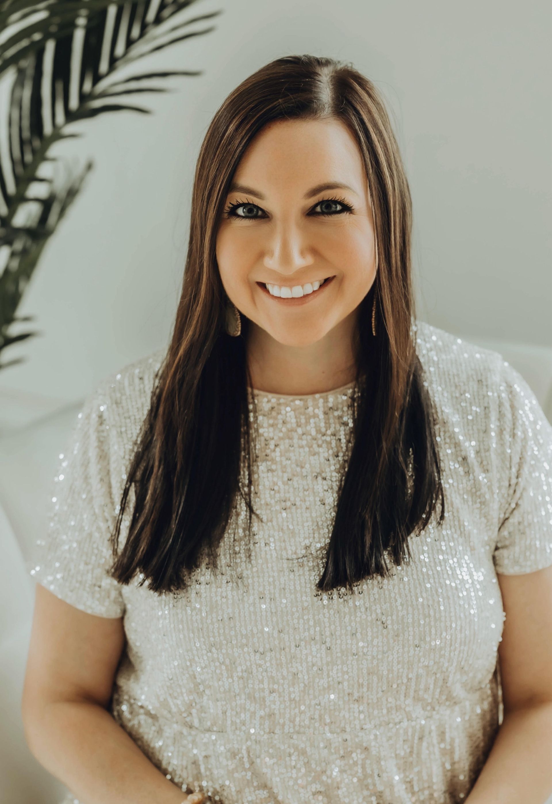 Smiling person in a sparkly light-colored top against a bright indoor background