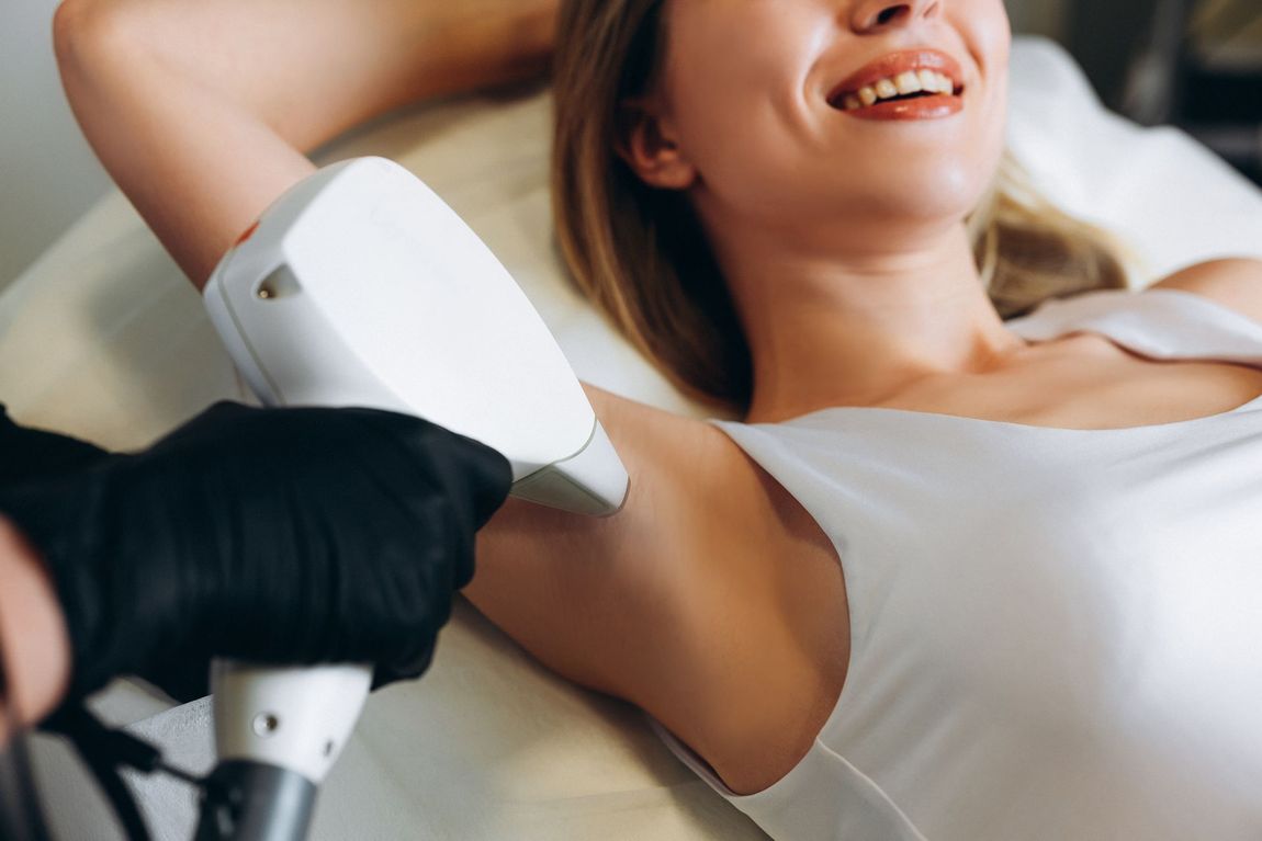 Woman receiving underarm laser treatment with a handheld device while lying on a treatment bed