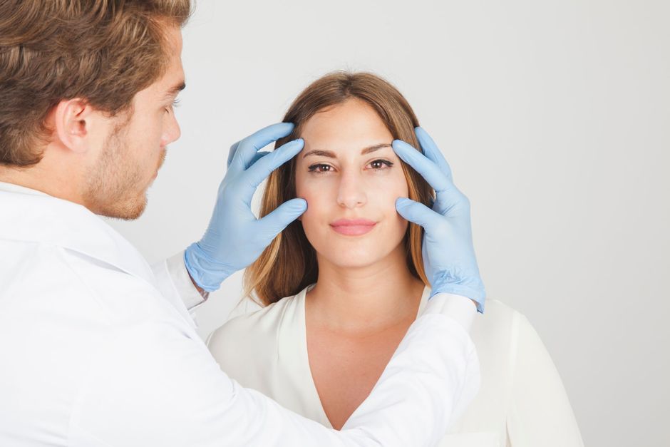 Doctor examining patient’s face with gloved hands in a bright clinic setting