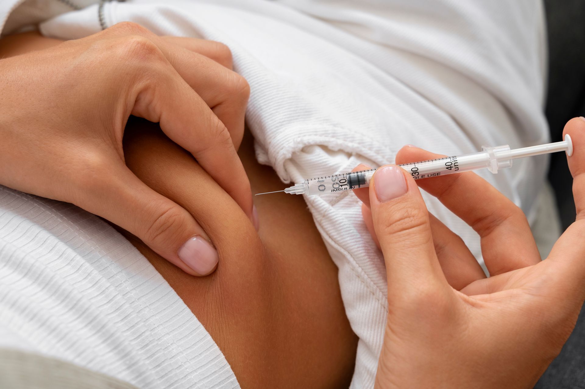 Health worker administering an injection into a person’s upper arm through a white sleeve