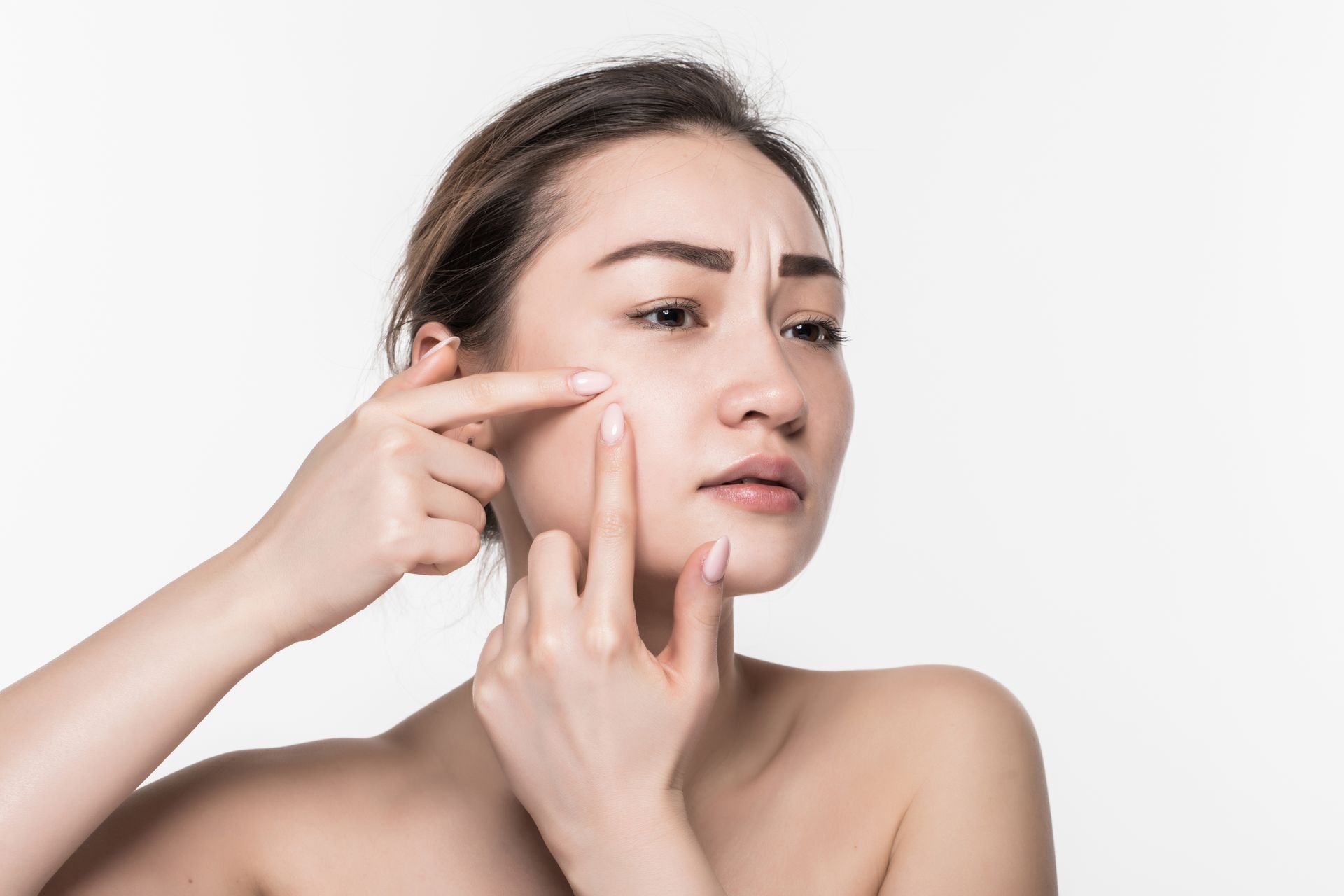 Woman touching her cheek beside a visible facial blemish, examining skin against a plain white background