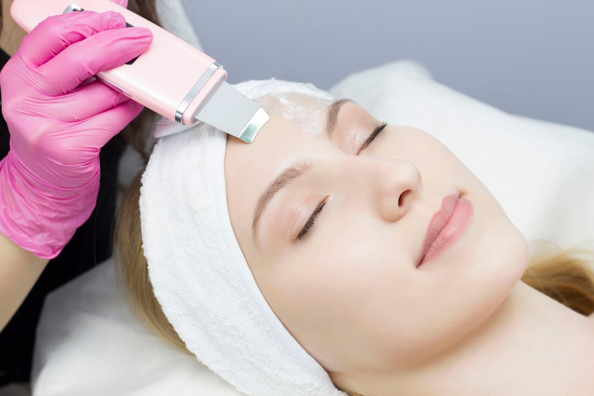 Gloved hand using a facial treatment device on a woman with a headband in a spa setting