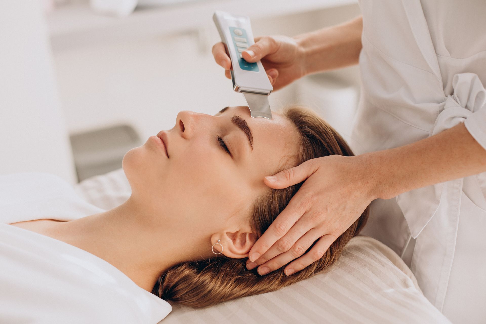 Cosmetic facial treatment with a handheld device at a spa, woman lying relaxed on a treatment bed