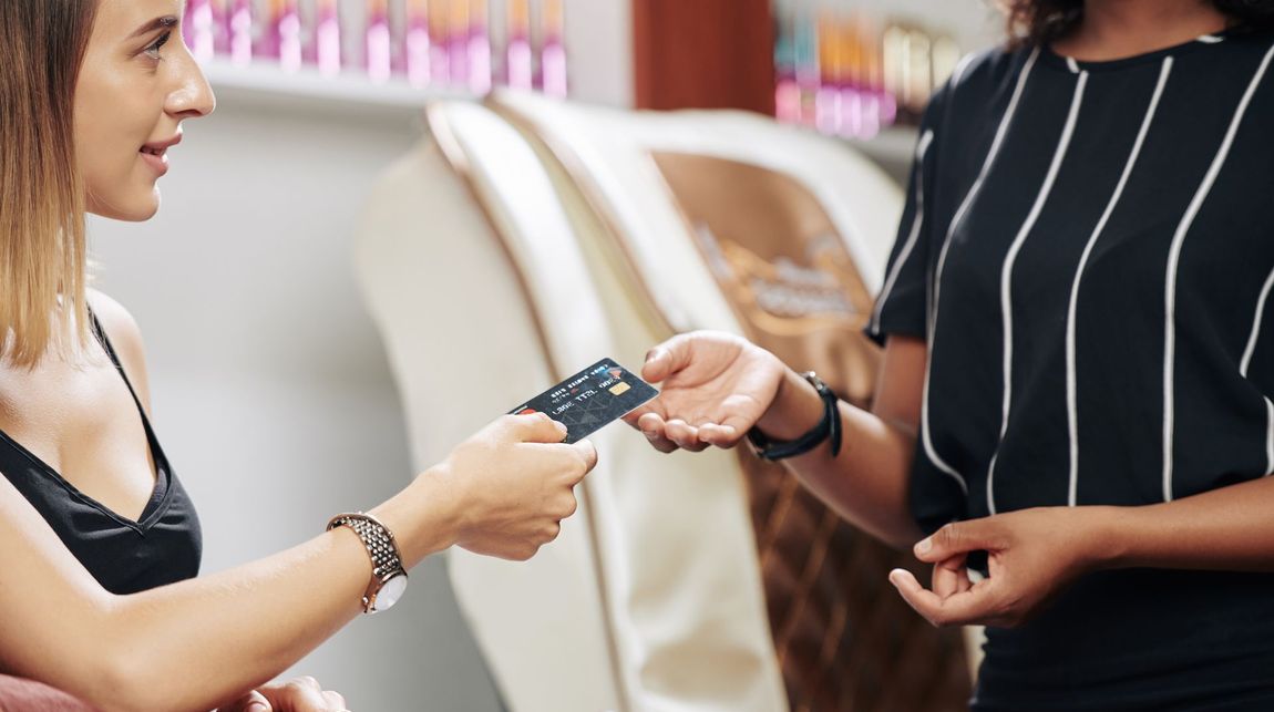 a woman is giving a credit card to another woman in a salon .