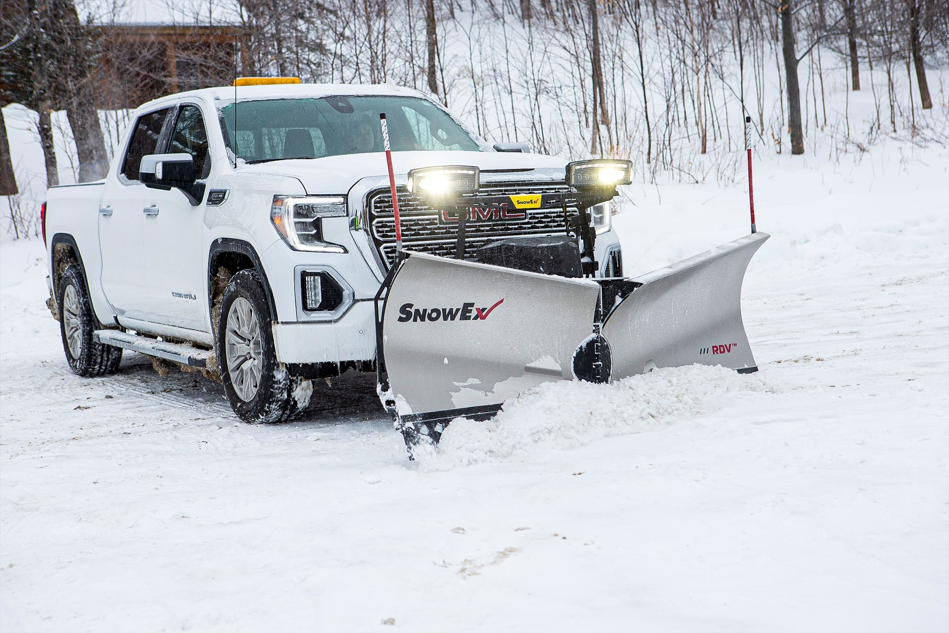 White truck with snow plow clearing snow from a driveway.