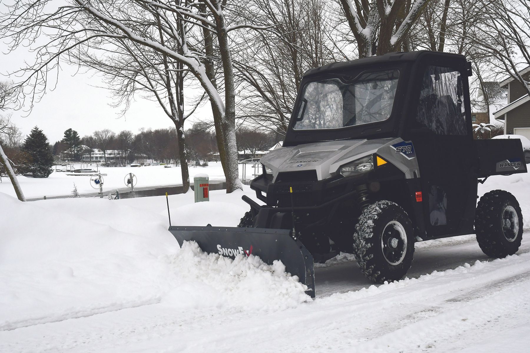 UTV with snow plow clearing snow from a road on a winter day.