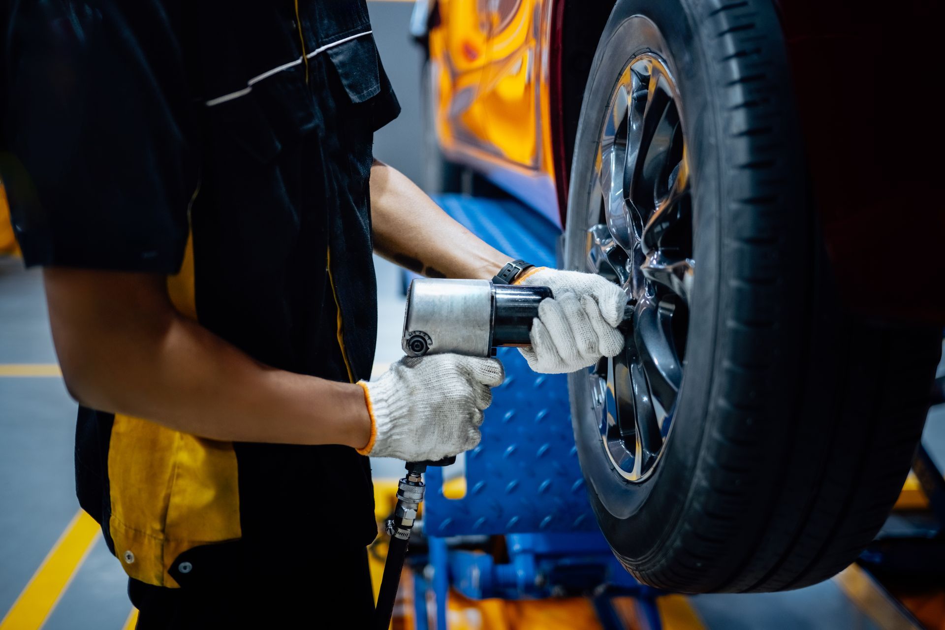 Mechanic using a pneumatic wrench to remove a tire from a car on a lift.