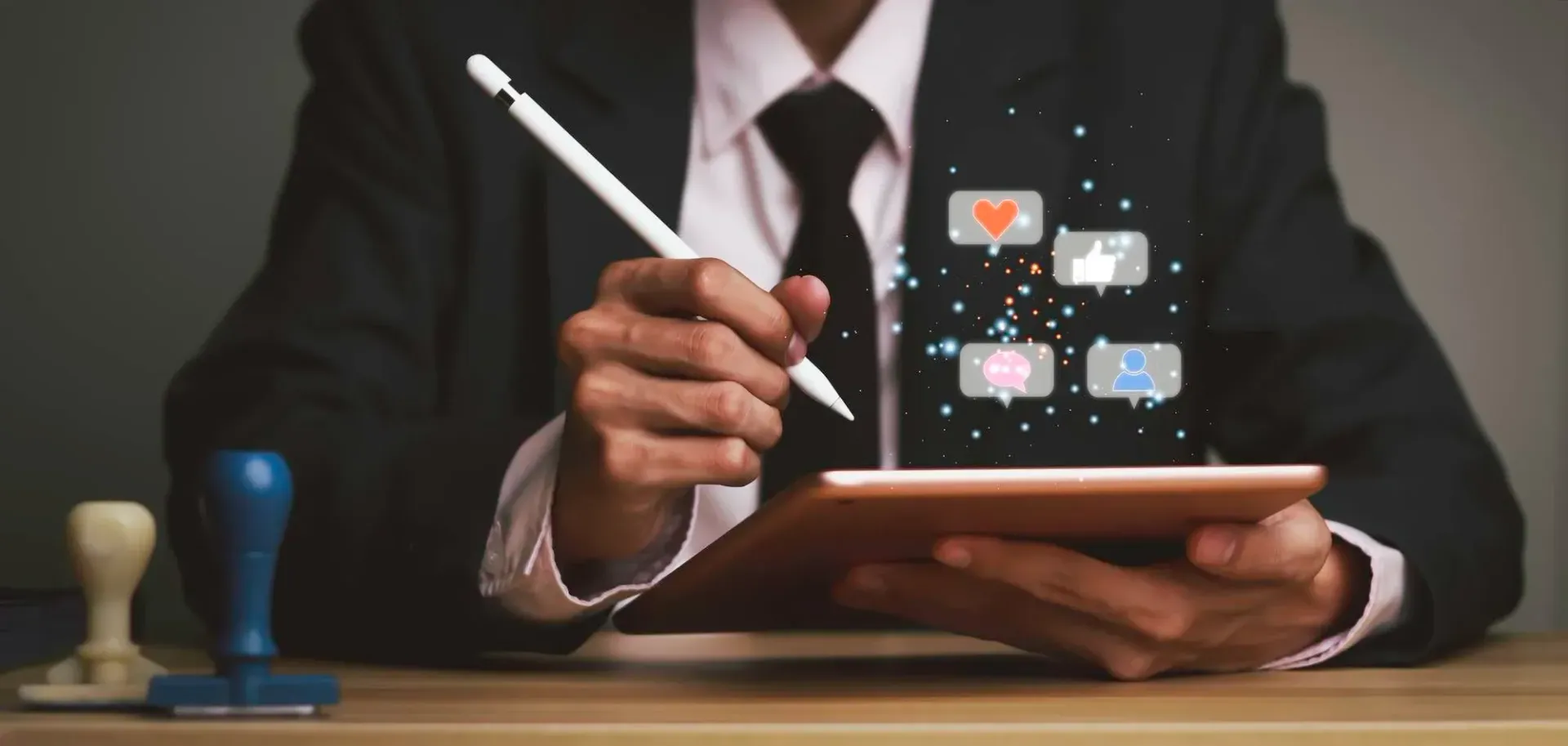 Une personne en costume utilise un stylet sur une tablette, avec des icônes de réseaux sociaux numériques flottant au-dessus de l'écran.