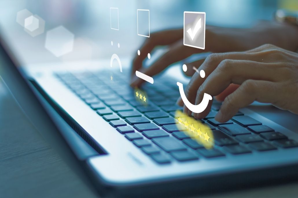 Des mains tapent sur un ordinateur portable avec une superposition numérique affichant des icônes de commentaires clients allant de « insatisfait » à « très satisfait ».
