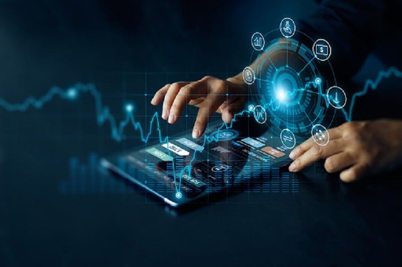 Les mains interagissent avec une tablette affichant des graphiques et des icônes financières numériques lumineux sur un fond sombre et high-tech.