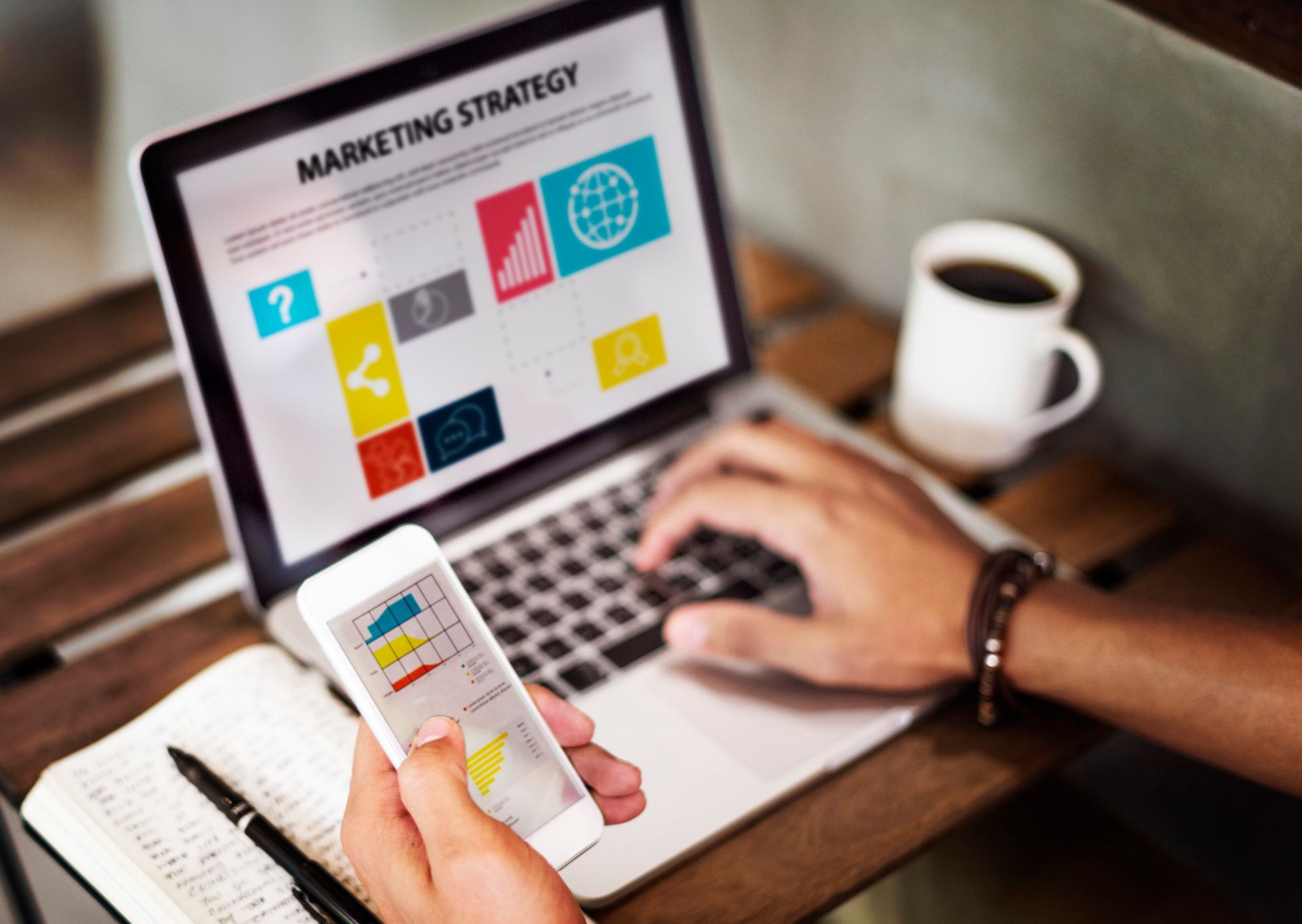 Une personne utilise un ordinateur portable affichant une présentation de stratégie marketing tout en tenant un smartphone contenant des graphiques de données.