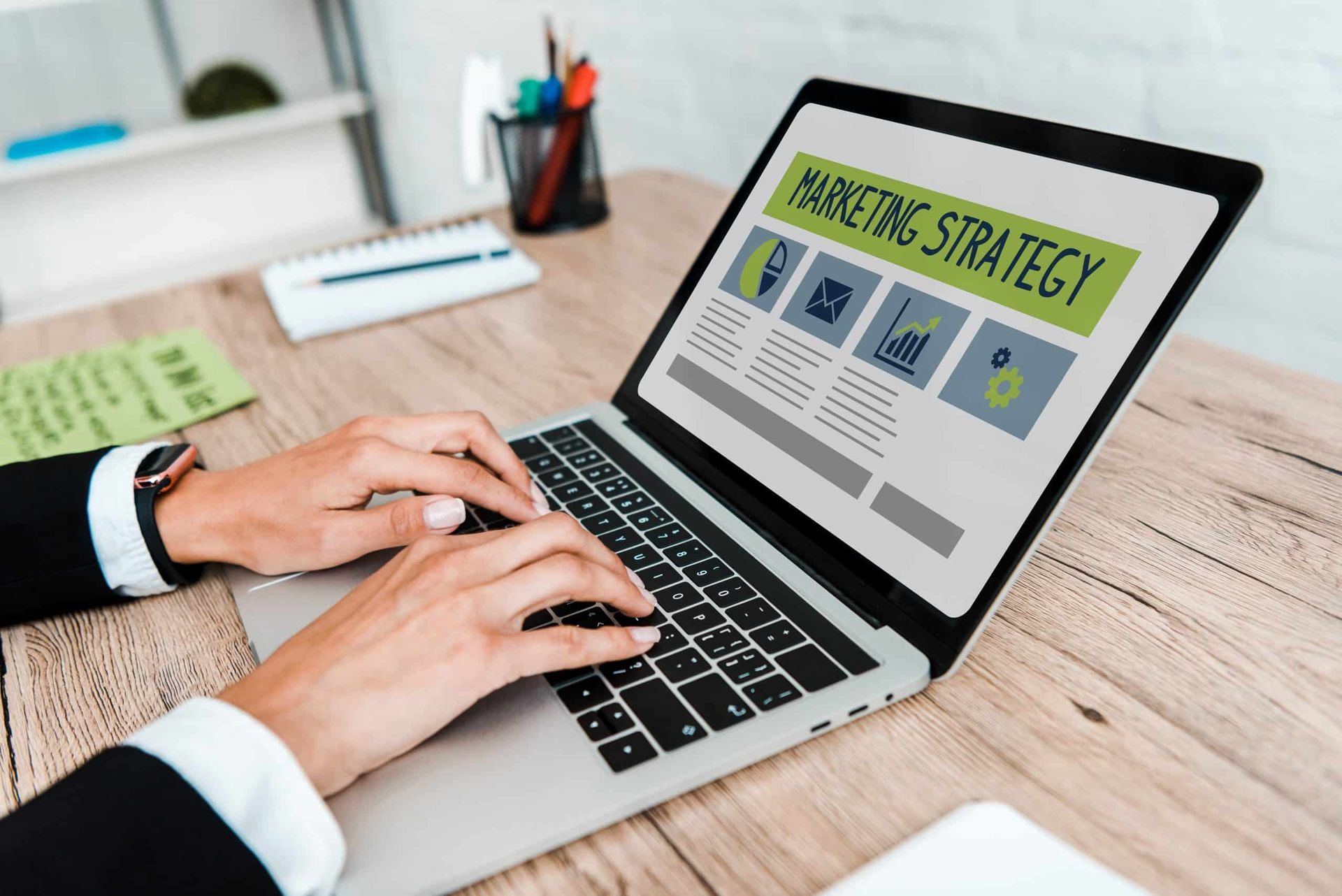 Une personne en costume tape sur un ordinateur portable affichant une présentation de stratégie marketing sur un bureau en bois.