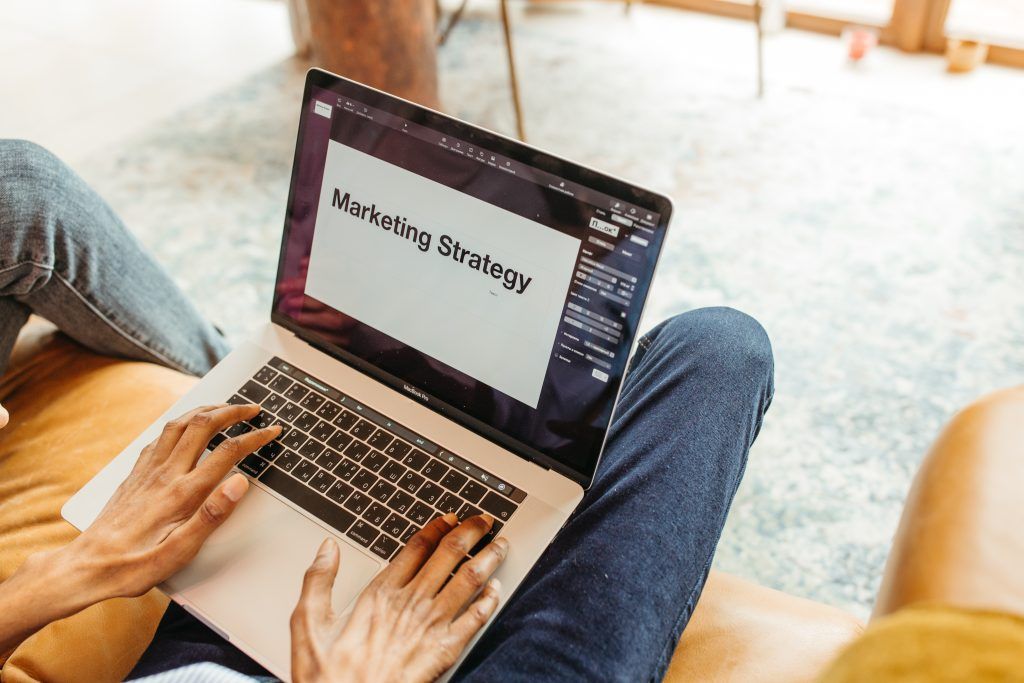 Des mains tapant sur un ordinateur portable affichant le texte « Stratégie marketing » sont posées sur les genoux.
