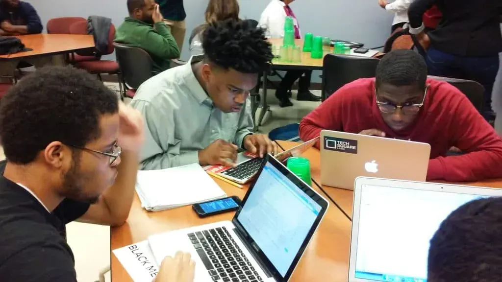 Les élèves se concentrent sur leurs ordinateurs portables et leurs feuilles de papier, assis à une table, pendant une activité de groupe en classe.