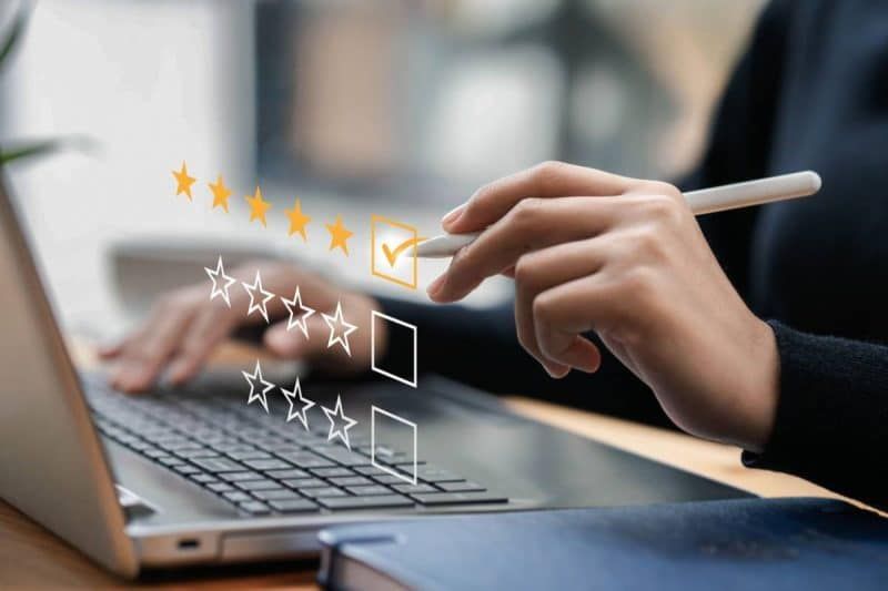 Une personne utilise un stylet pour sélectionner une note de cinq étoiles sur une interface virtuelle tout en travaillant sur un ordinateur portable.