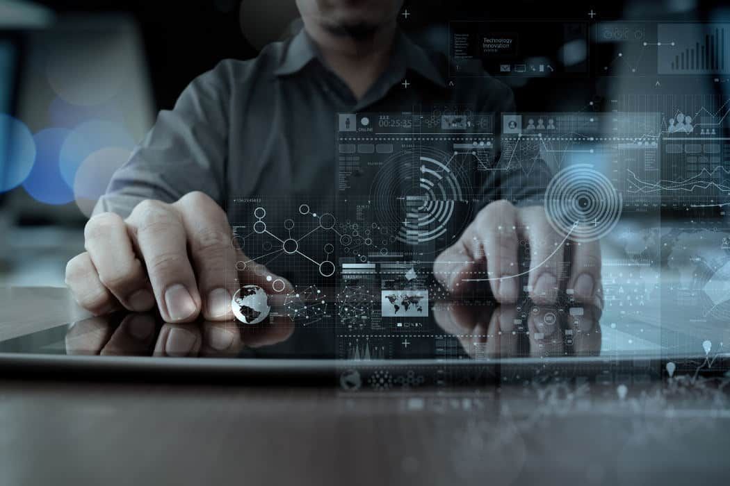 Les mains d'une personne interagissant avec une tablette numérique affichant des interfaces de données holographiques et des analyses globales.