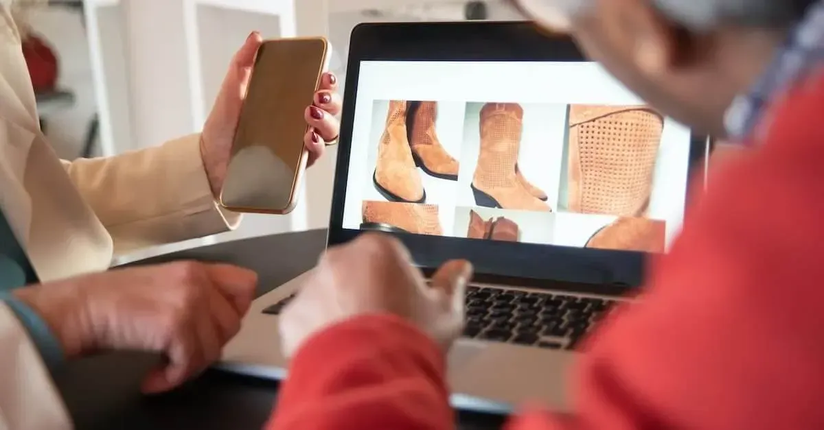 Deux personnes en tenue professionnelle consultent des images de bottes beiges sur un ordinateur portable tout en tenant un smartphone.