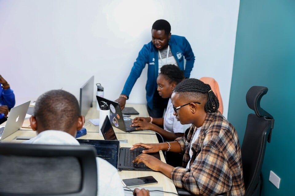 Dans un bureau moderne, des collègues collaborent sur des ordinateurs portables à un bureau partagé, tandis qu'un membre de l'équipe leur apporte son aide.