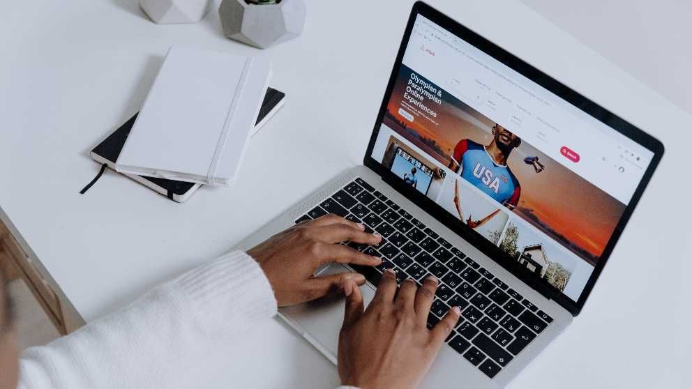 Une personne tape sur un ordinateur portable posé sur un bureau blanc, un carnet à portée de main.